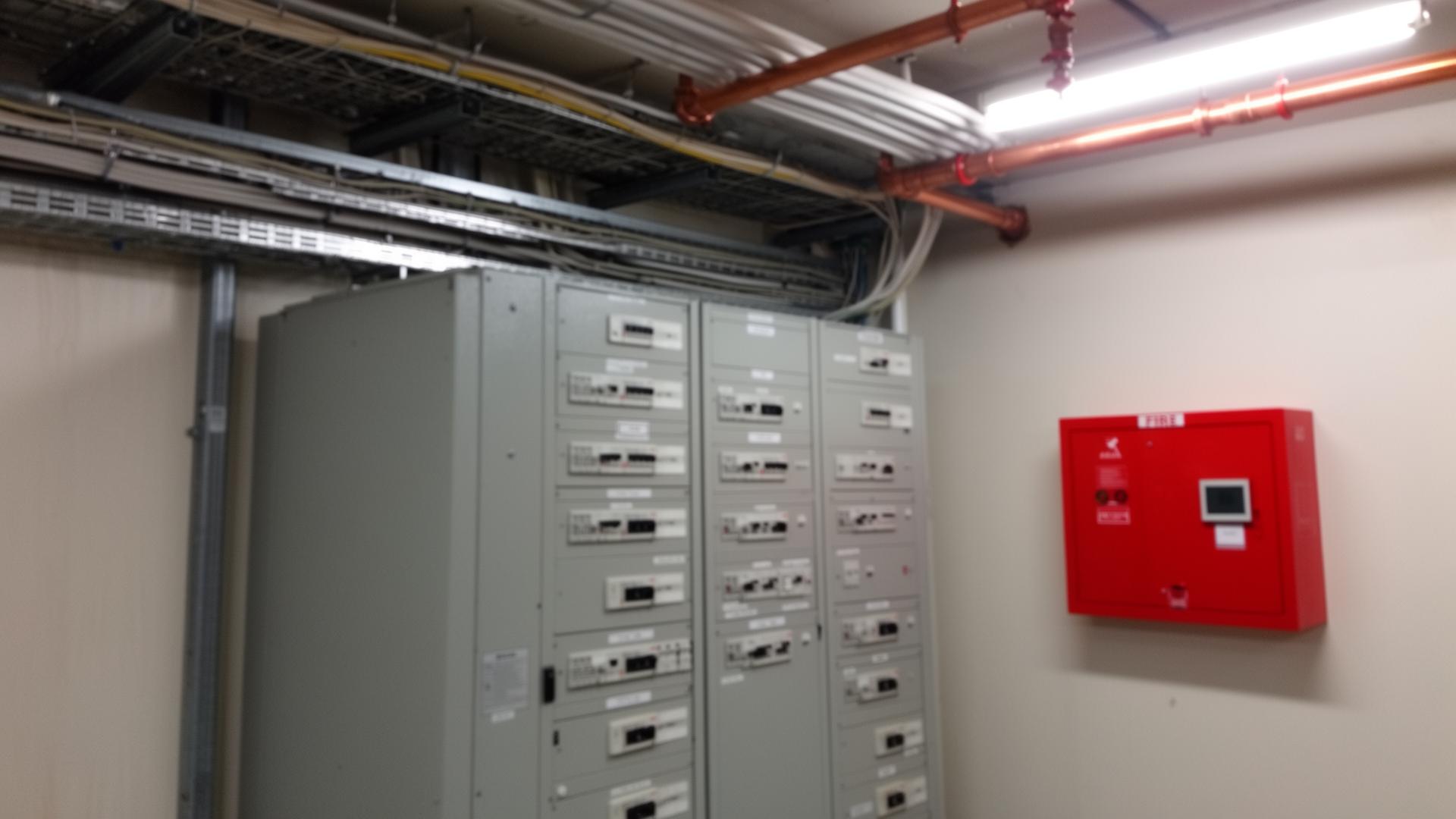 Commercial switchboard room with labelled circuits, fire indicator panel and EXIT signage on an Australian site — ISO 45001 certification for electrical and fire services contractors