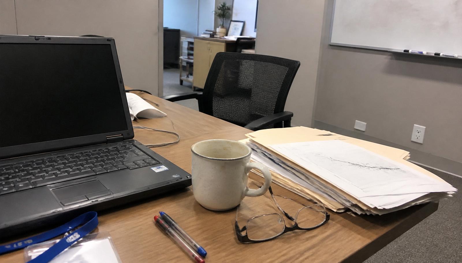 Consultant's desk with laptop, client files, reading glasses and a lanyard in an Australian office — ISO 9001 certification for professional services firms